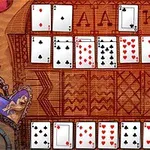Rozložené hrací karty s převážně červenými a černými symboly na dřevěném podkladu s ornamenty