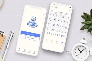 Dva mobilní telefony s aplikací pro řešení sudoku, keramická figurka sovy a rostlina na bílém pozadí