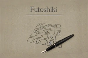Plnicí pero leží na papíře s číselnou mřížkou a nadpisem Futoshiki
