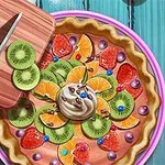Ovocný koláč zdobený plátky kiwi, pomeranči, jahodami, šlehačkou a čokoládovými kousky vedle kuchyňské desky