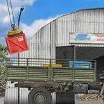 Bílý nákladní vůz zaparkovaný před skladištěm s jeřábem zvedajícím červený kontejner