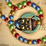 Černá soška s otevřenými ústy a barevné koule na pozadí s egyptskými motivy